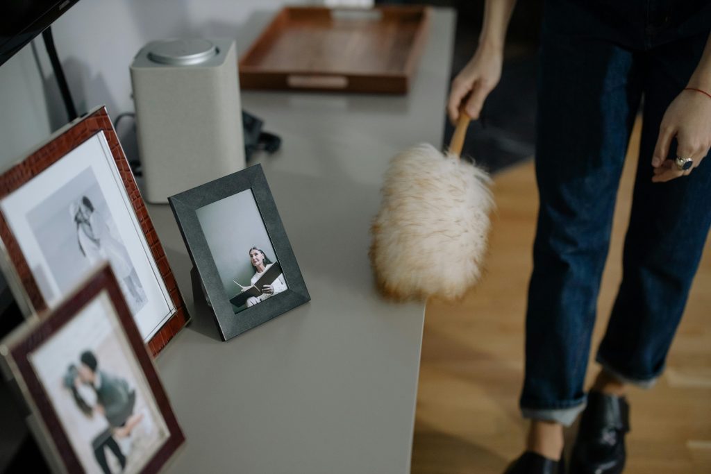 woman dusting a shelf with framed prints